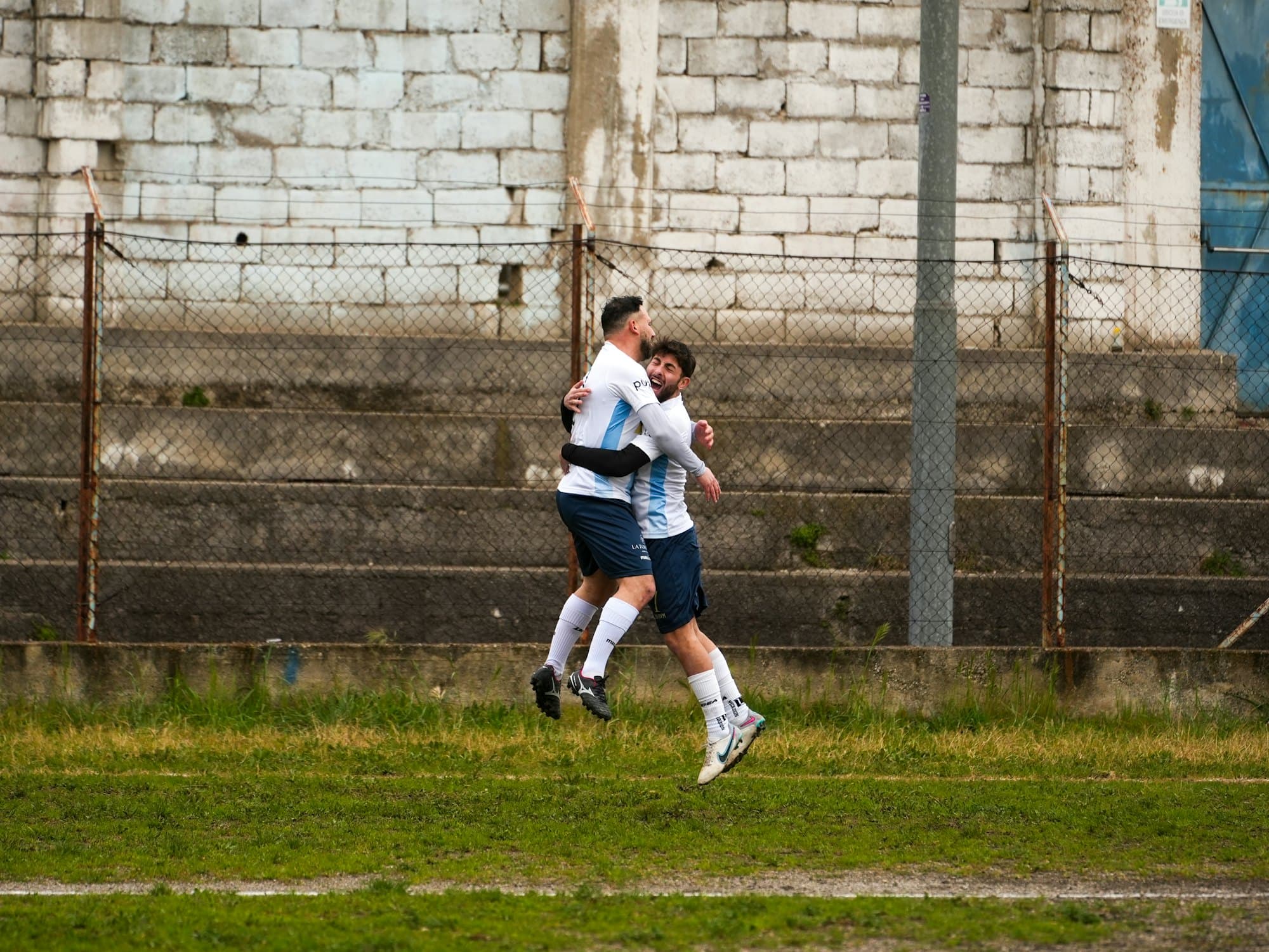 Deux footballeurs en blanc et bleu ciel se sautent dans les bras après un but