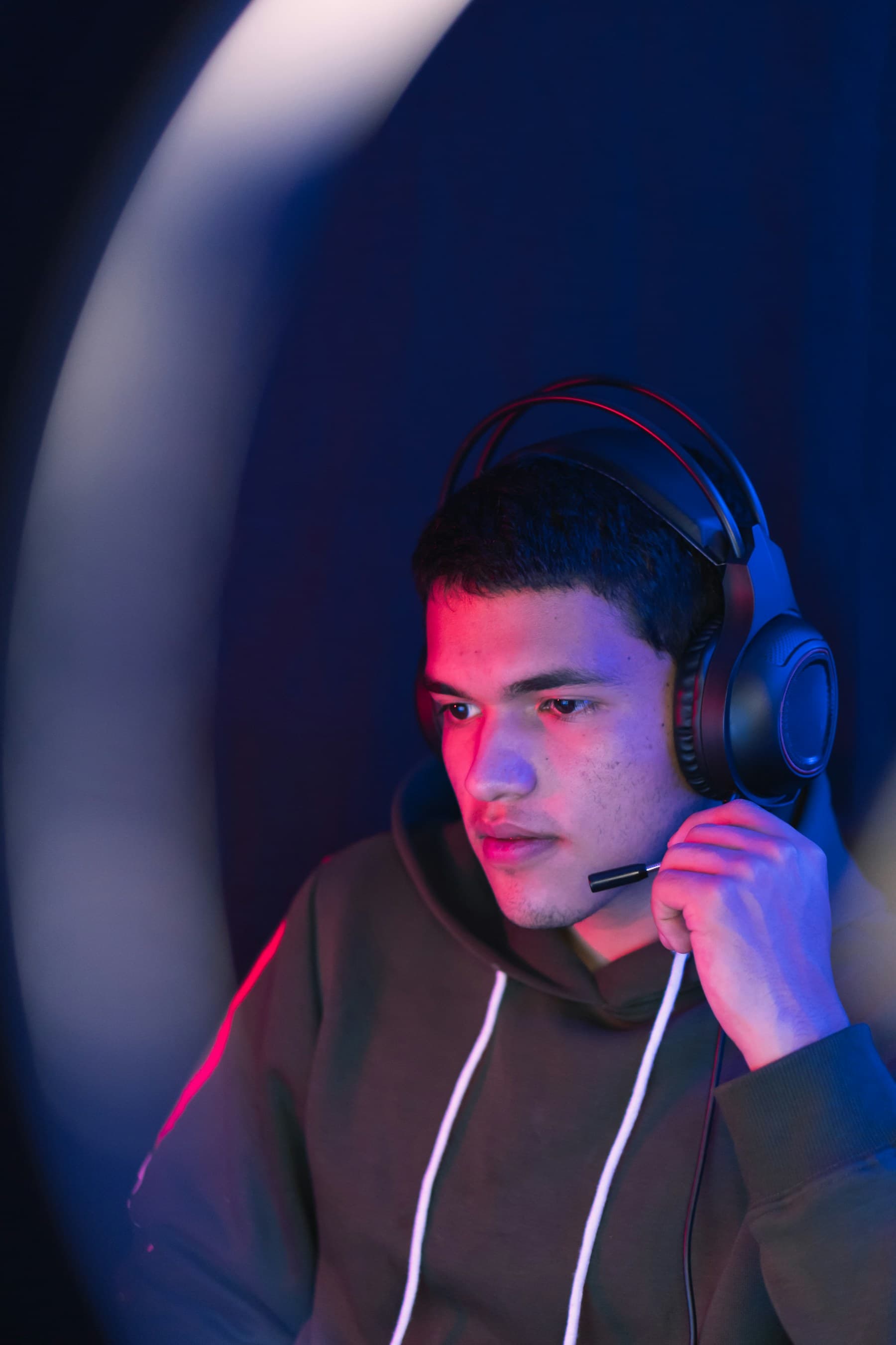 Joueur d’esport concentré, casque sur les oreilles, éclairé en rouge et bleu